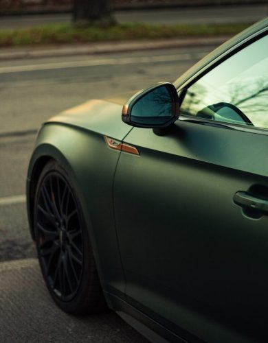 Matte dark green car parked on asphalt street.